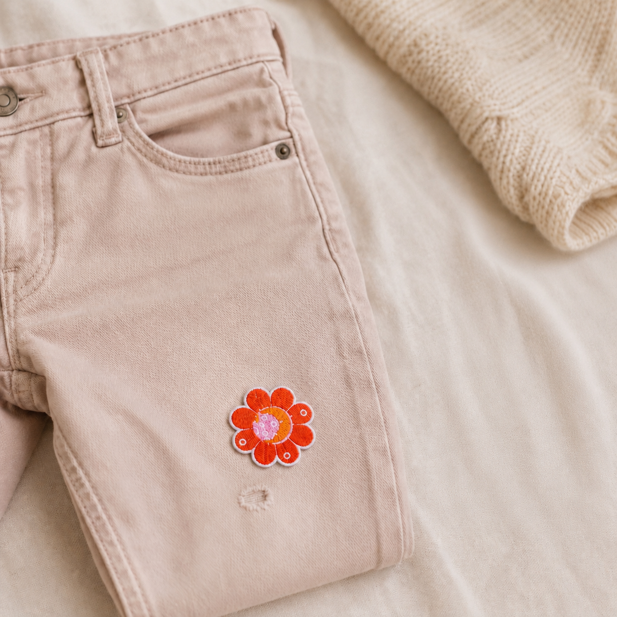 Orange blomster strygemærke på lyserøde jeans ved et lille hul i stoffet. Det broderede, påstrygelige stofmærke er velegnet til at reparere huller i bukser eller give jeans og andet tøj et personligt udtryk.