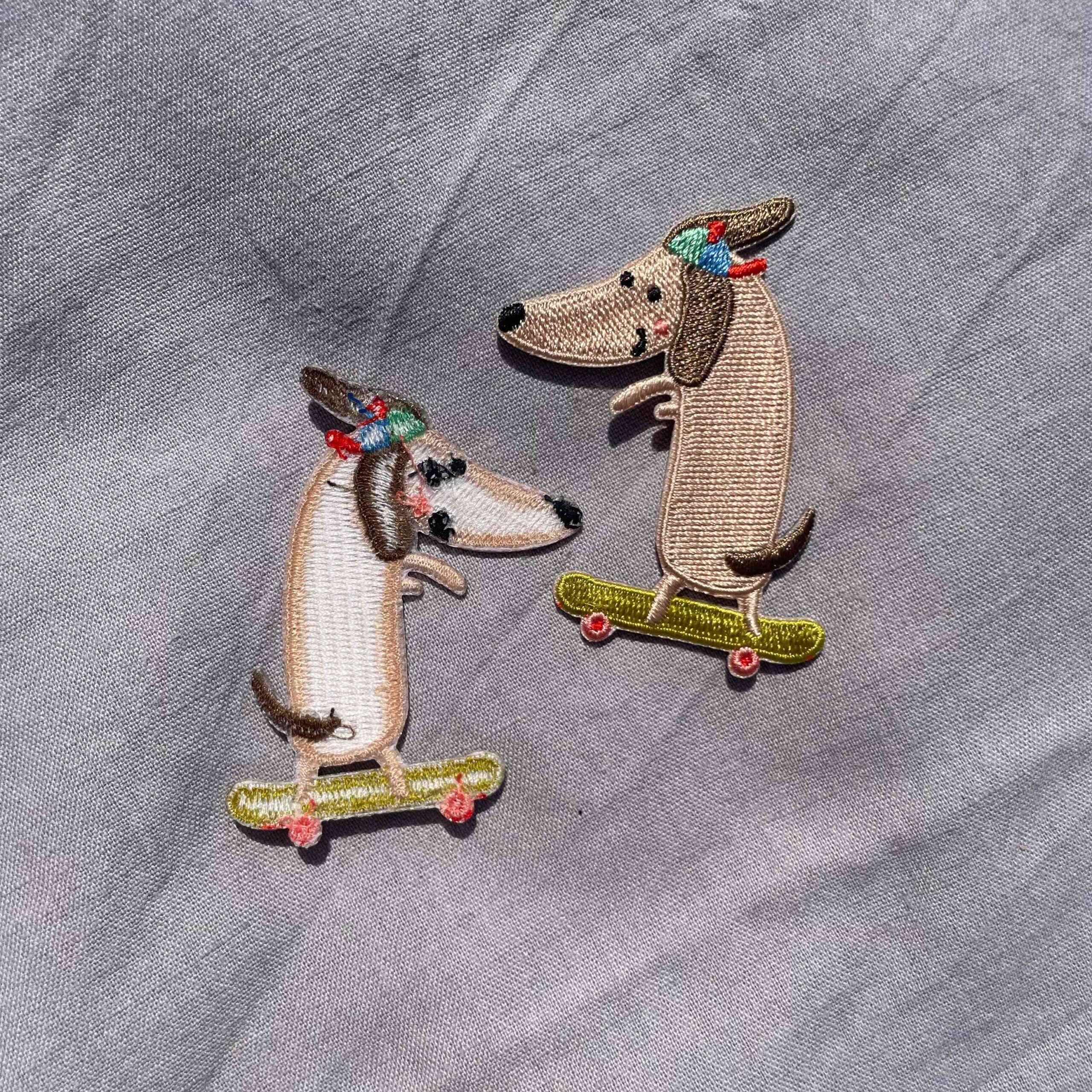 To broderede strygemærker med gravhunde på skateboard iført farverige kasketter. Ideelle til at reparere huller eller dekorere jakker, jeans, børnetøj, tasker og accessories.