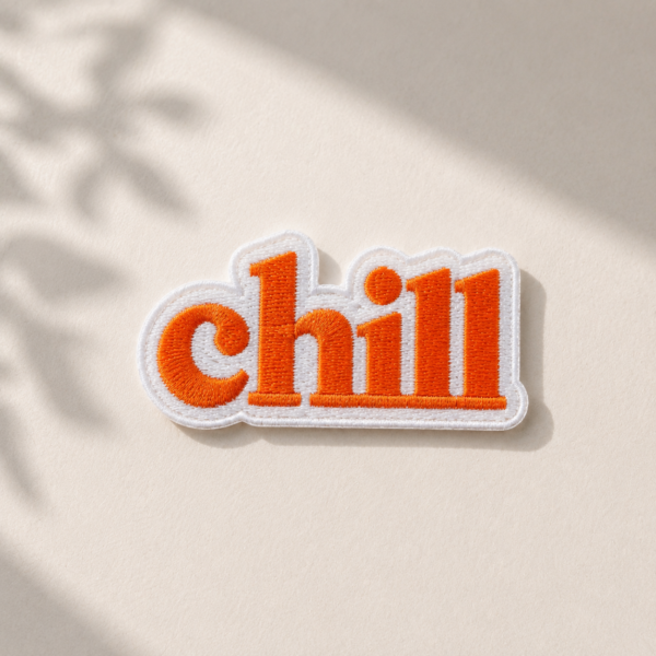 Broderet Chill strygemærke i orange og hvid på lys baggrund med naturligt lys. Iron-on patch til reparation og personliggørelse af jakker, jeans, tasker og andet tøj.