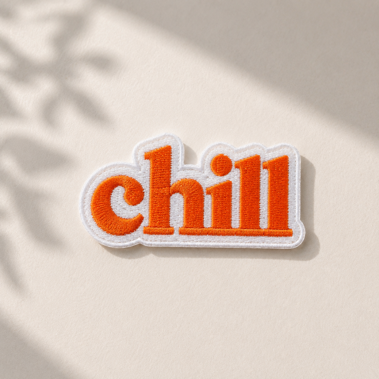 Broderet Chill strygemærke i orange og hvid på lys baggrund med naturligt lys. Iron-on patch til reparation og personliggørelse af jakker, jeans, tasker og andet tøj.
