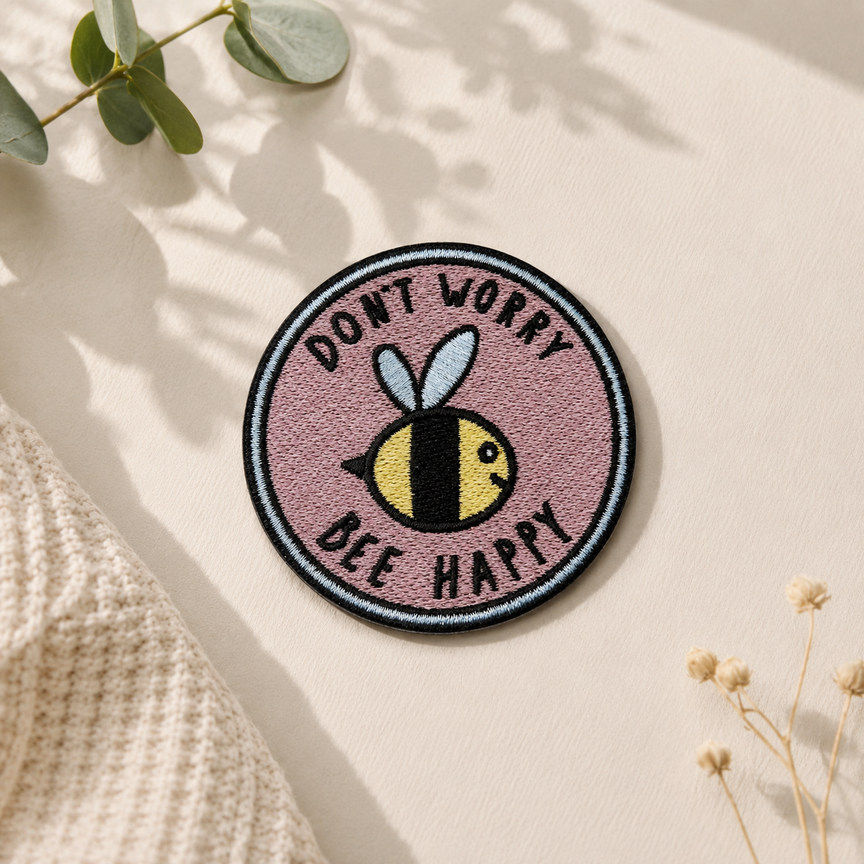 Broderet Don't Worry Bee Happy strygemærke med gul bi på rosa baggrund. Rundt iron-on patch til jakker, tasker, jeans og andet tøj. Ø 7 cm.