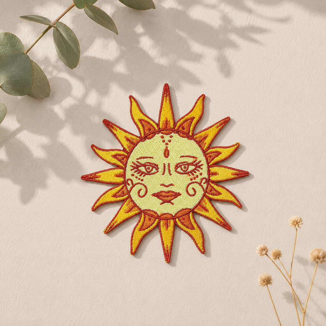 Broderet sol strygemærke med boho-inspireret soldesign i gule og orange nuancer på lys baggrund med naturligt lys. Iron-on patch til jakker, tasker og andet tøj.